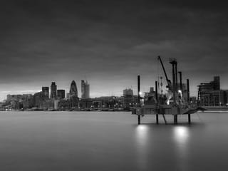 Black and white photograph of a cityscape in front of a large body of water.