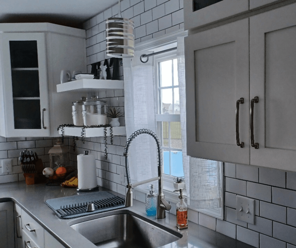 A beautiful grey and white kitchen with gray counter tops. The sink and cabinets are highlights of the work BiiLT did for this project.