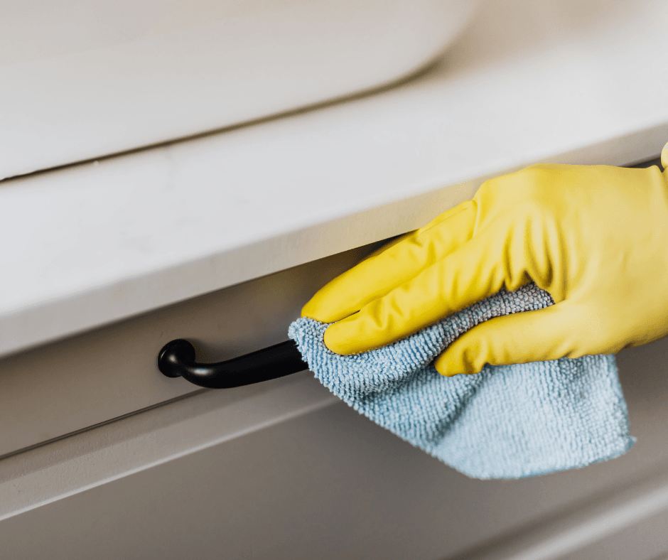 Picture of someone cleaning a counter and handle in the foreground. Seems to be some sort of counter or sink area.