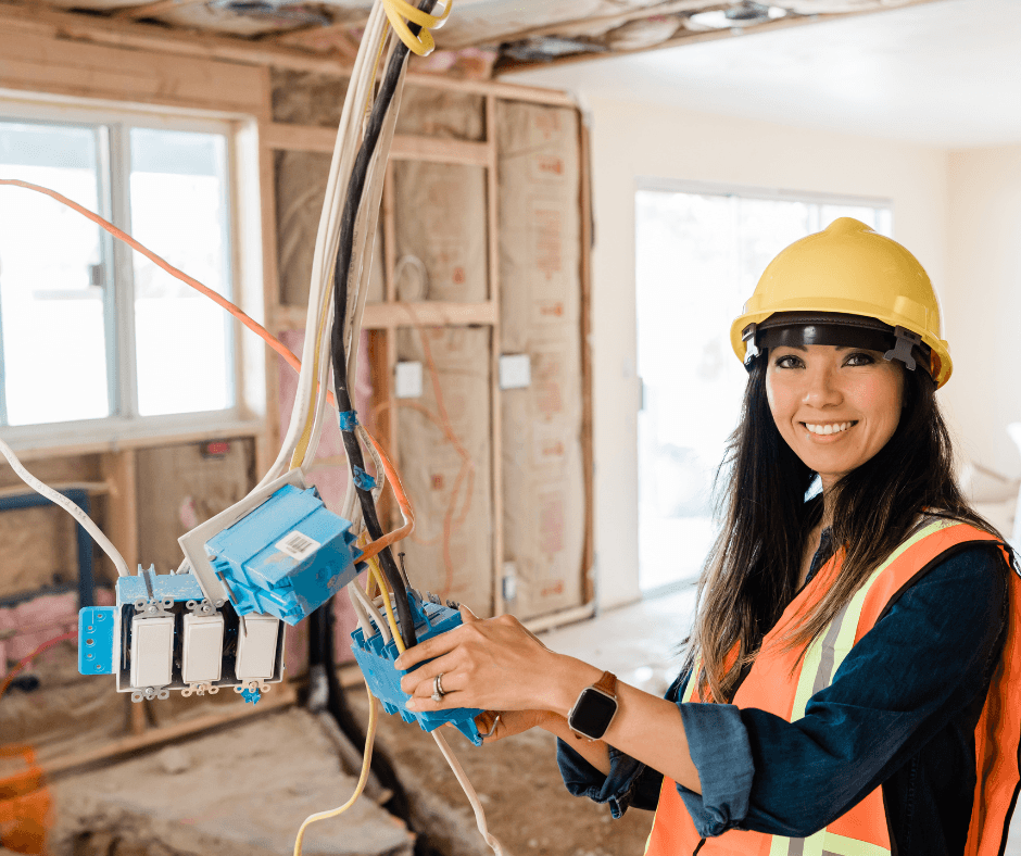 An electrician putting the finishing touches on some wiring. She's smiling and in the center of a half-built project.