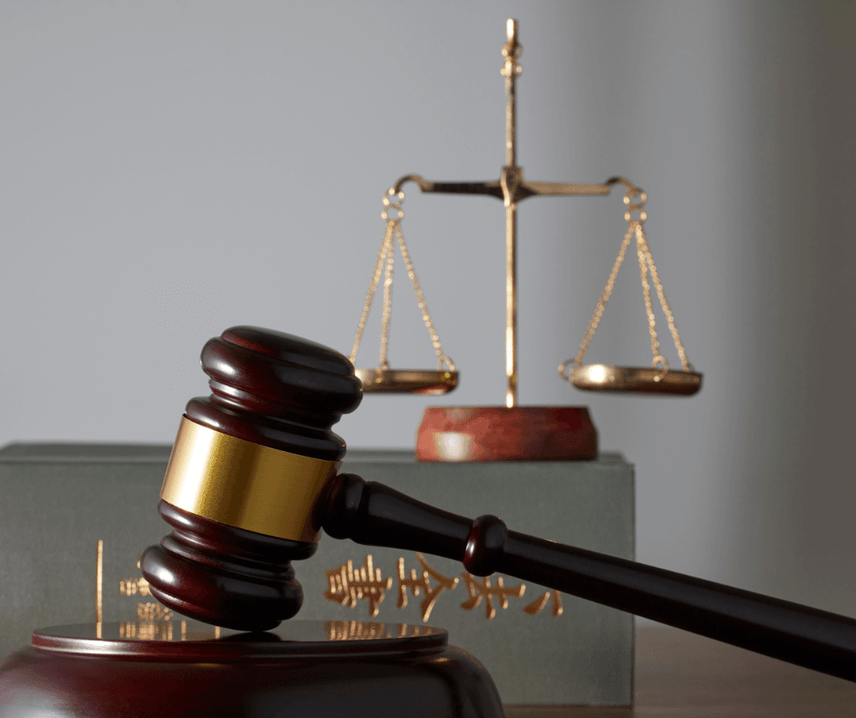 A legal gavel in the foreground of the image. In the background there is a scale.