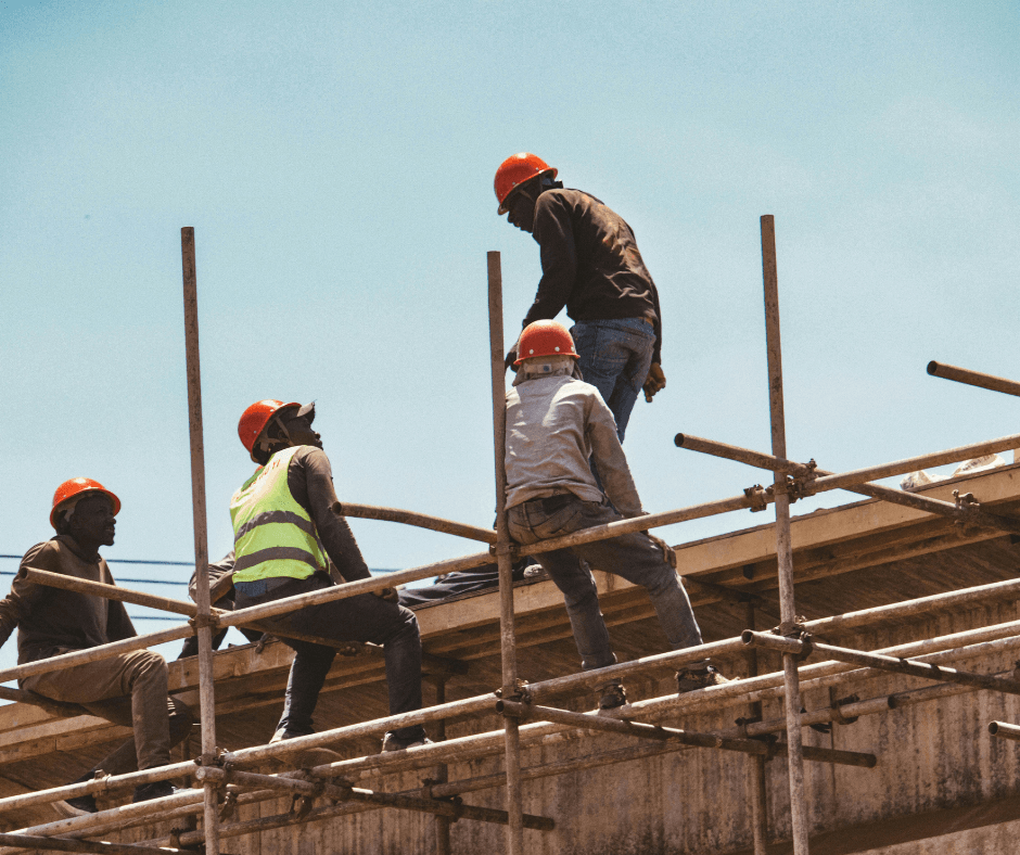 A group of four construction workers are resting on a scaffold built with poles. They seem to be mid conversation.