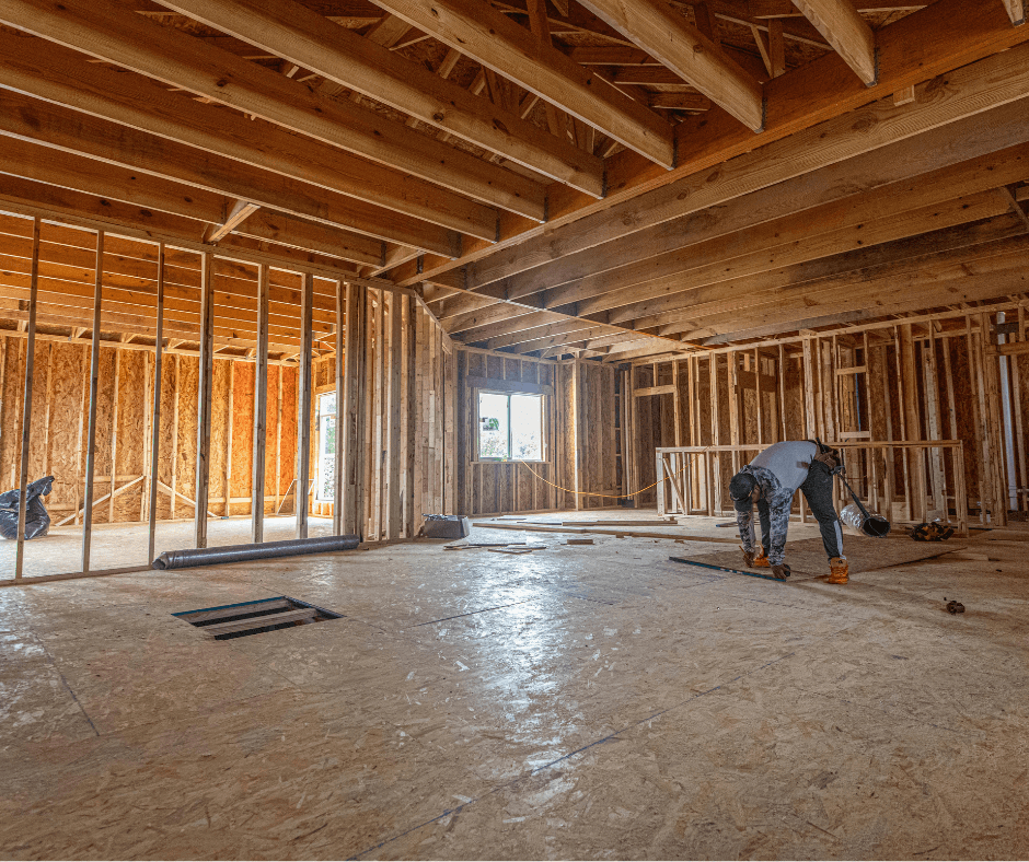 A wooden frame that has been almost completely set up. There is a worker in the right side finishing up what seems to be a wooden panel. Wooden framing example.