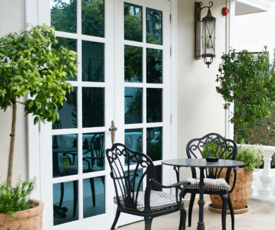 A Canva picture of an outdoor seating area on a patio. There seems to be a porch overhead, but it's cut off. There are two chairs and a table in the lower center, leaning to the right.