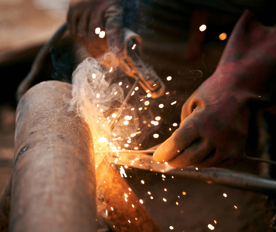 A picture of a pipe being wielded, with the person wearing personal protective equipment. Sparks are flying as the metal is merging into place.